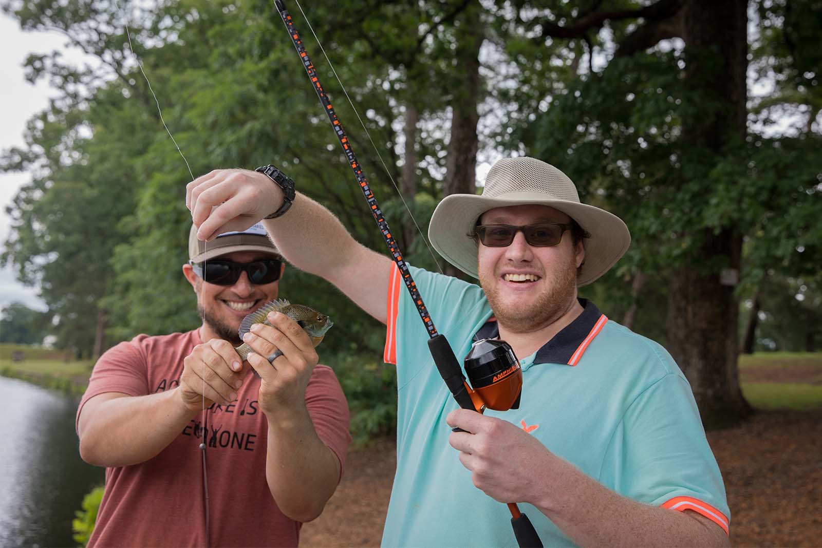 兩個男人站在一個湖泊的海岸線上。一個人拿著釣竿，另一個人則抱著從鉤子中取出的魚