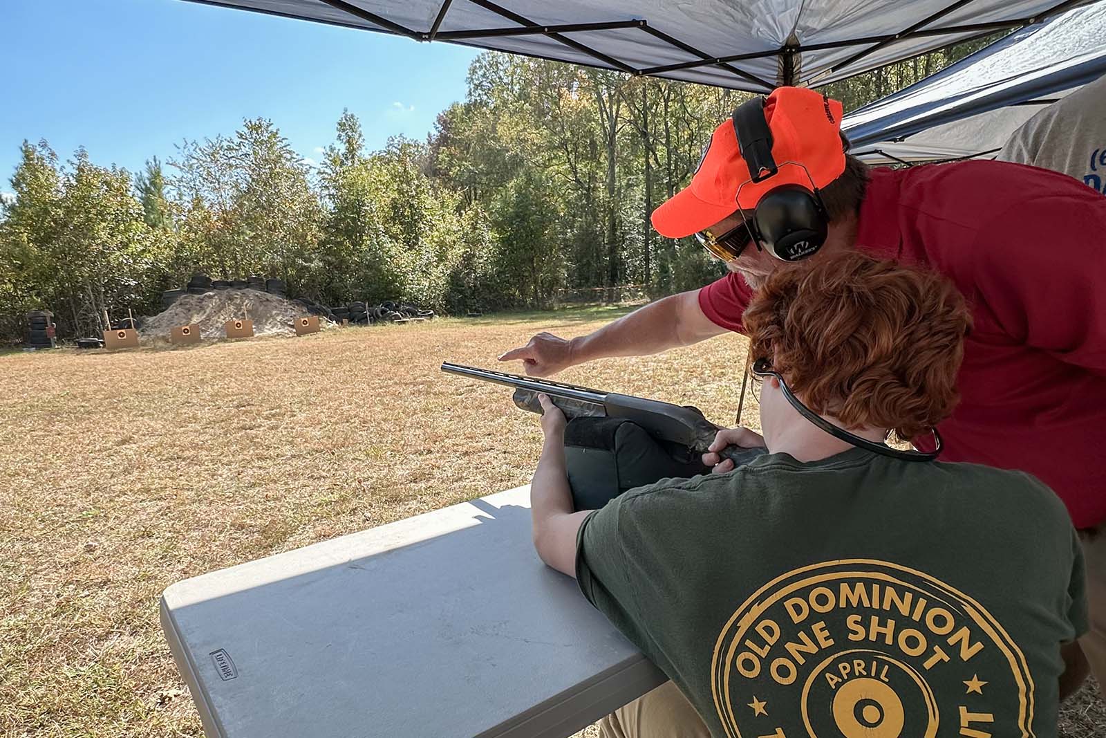 一個人用獵槍練習射擊目標；一位教練站在附近指向目標