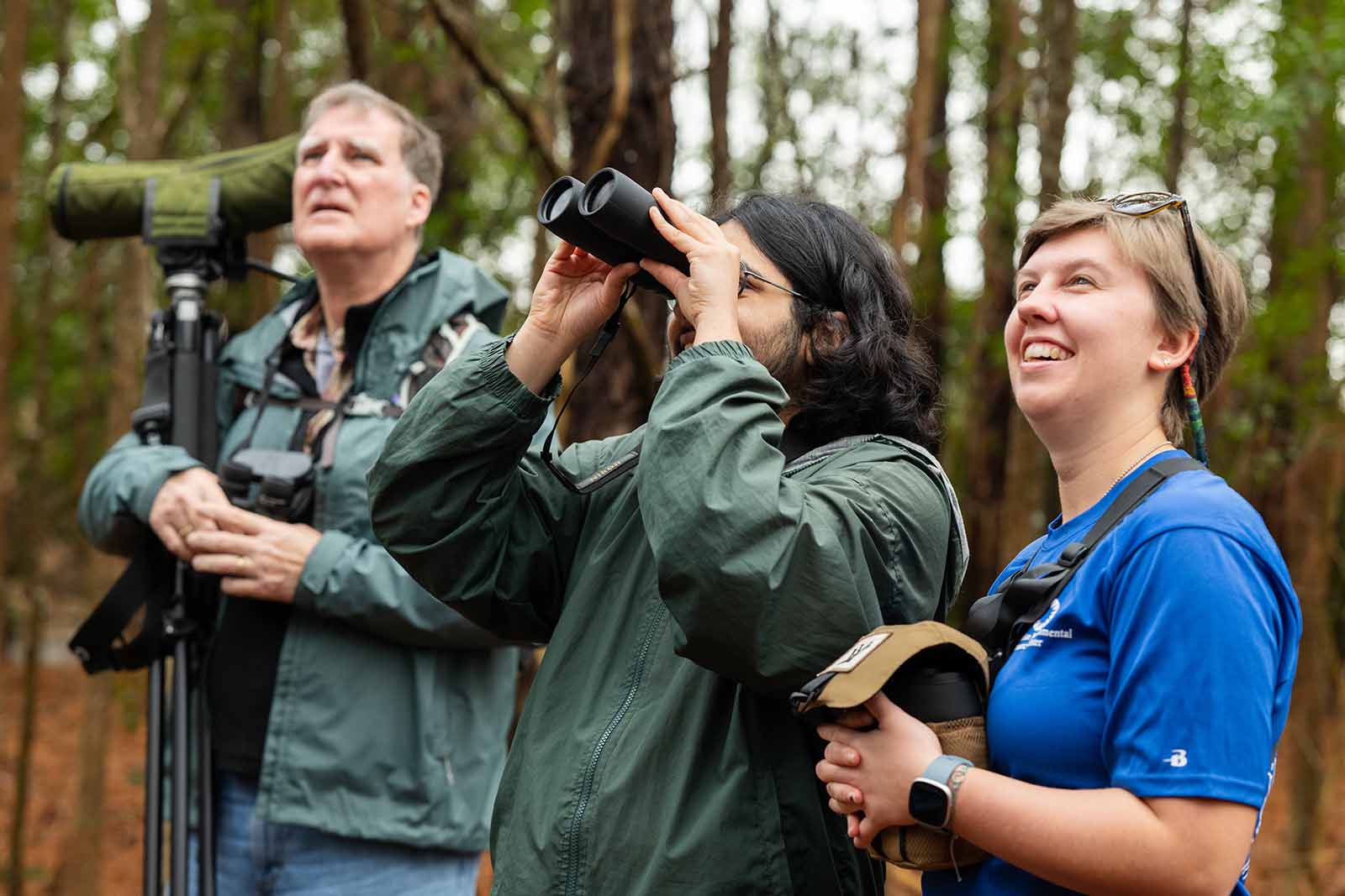 兩個穿著深綠色夾克的人向上看著，一人用雙望遠鏡