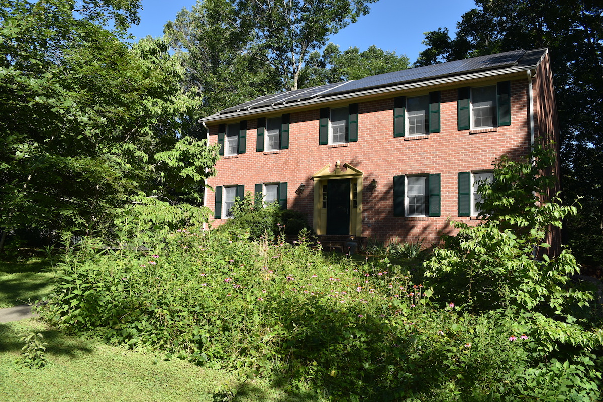 屋頂上有太陽能電池板的磚屋和前院的授粉花園的圖像