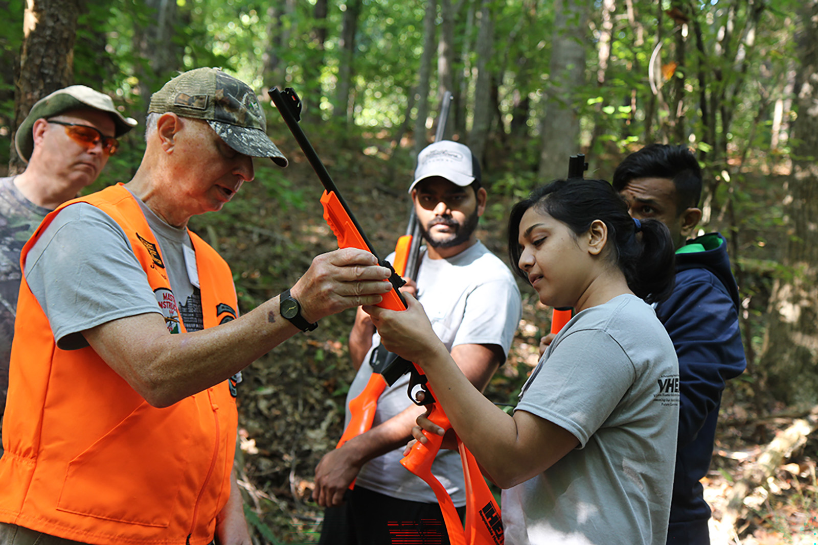 一名男子在一群人的注視下，向一名女子解釋如何握持獵槍的照片。