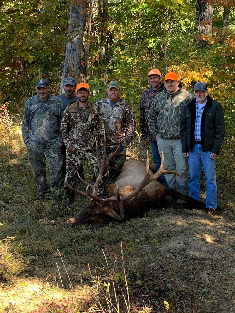 一群七個男子站在他們捕獲的公牛鹿旁