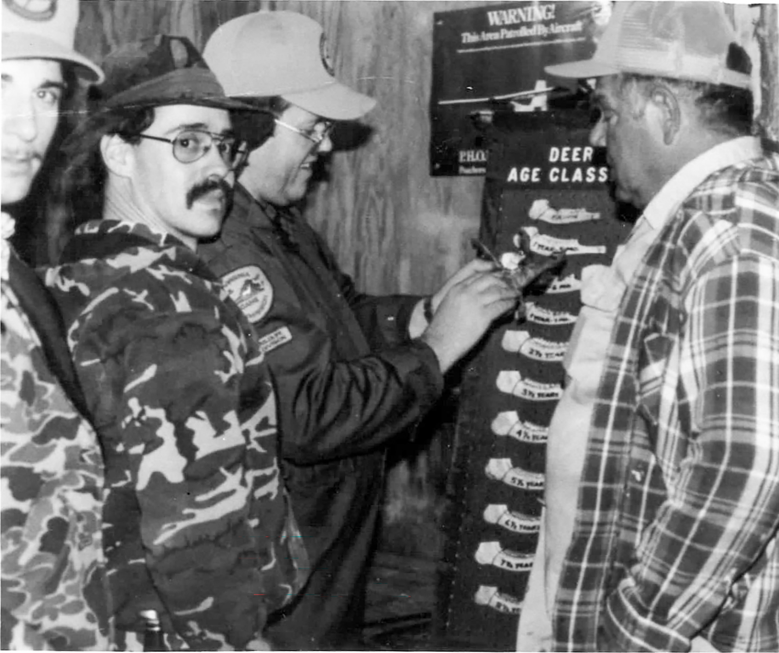 一張古老的黑白圖片，顯示獵人正在測量鹿的顎骨。