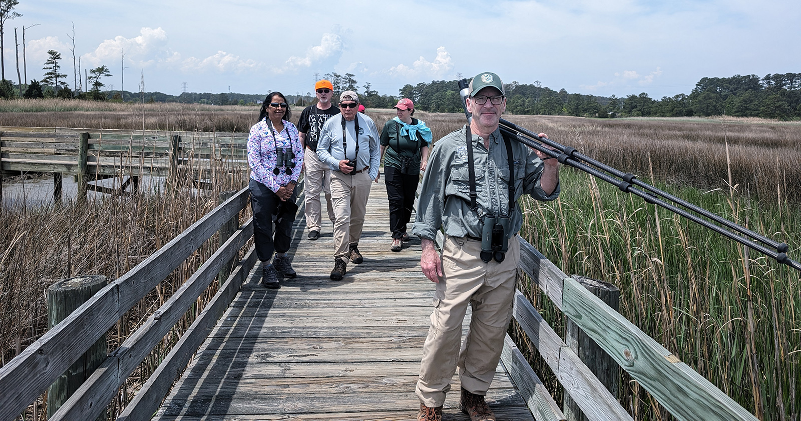 五個人戴雙筒望遠鏡在木板步道穿過濕地的照片。