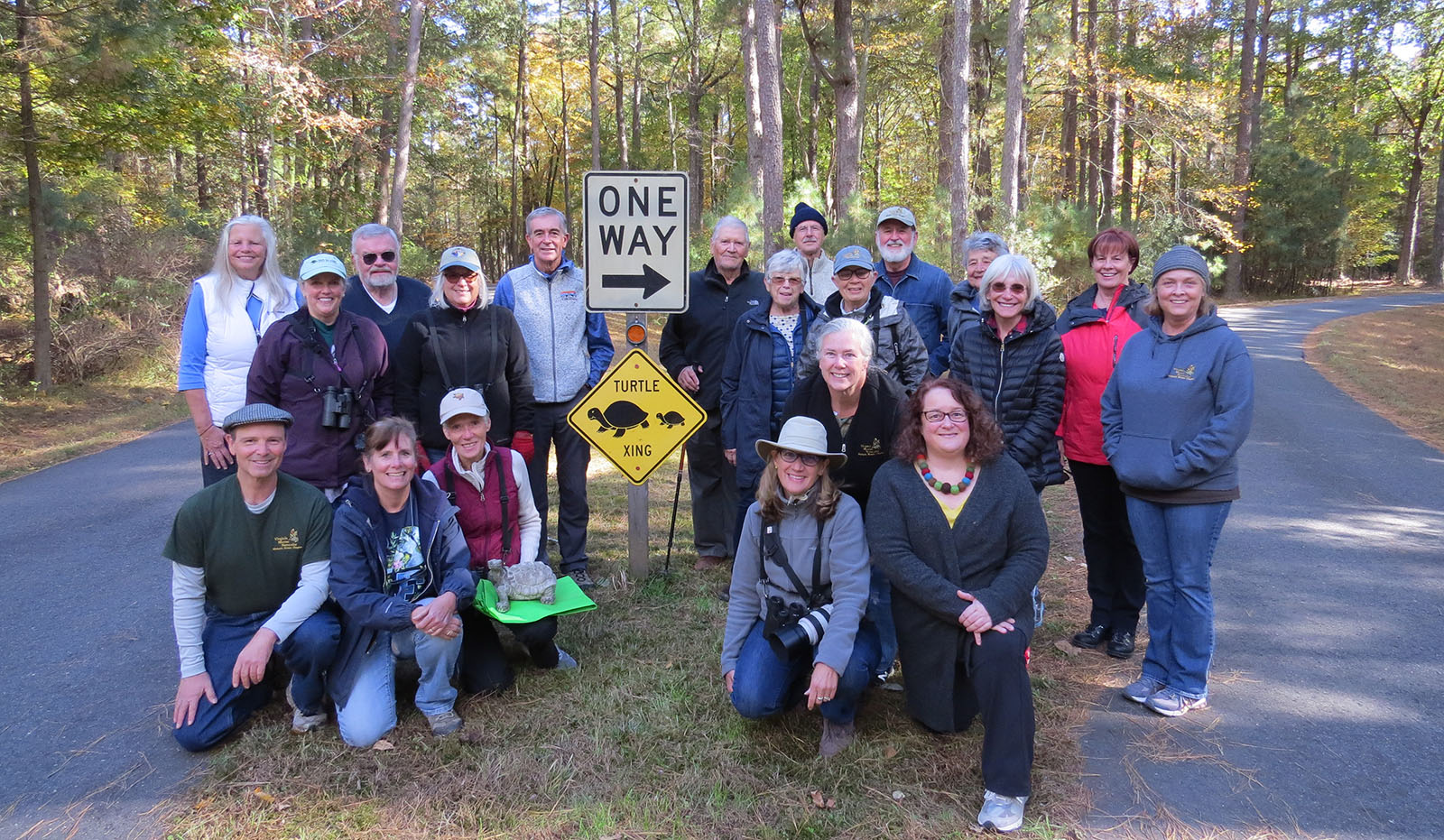 一群 20 人聚集在一條小路鋪路中間的海龜過渡標誌周圍,前面有一個人膝蓋著一隻烏龜雕像。