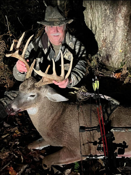 一位迷彩的男人，戴著弓，握著一隻收穫的大牛角的角子的照片。