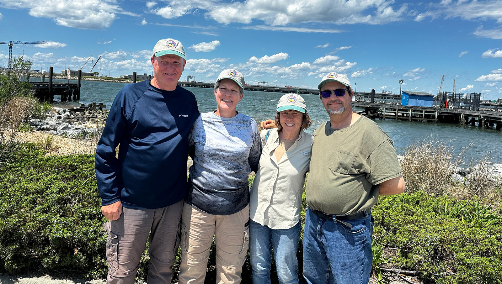 四個微笑的人站在背景有水的島上的海灘上的照片。