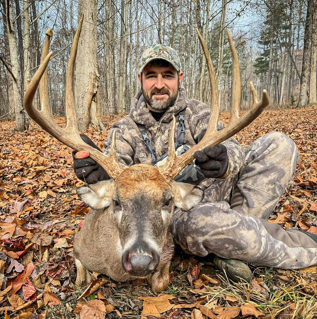 一個戴著迷彩的男人和一隻大型白尾鹿的照片。