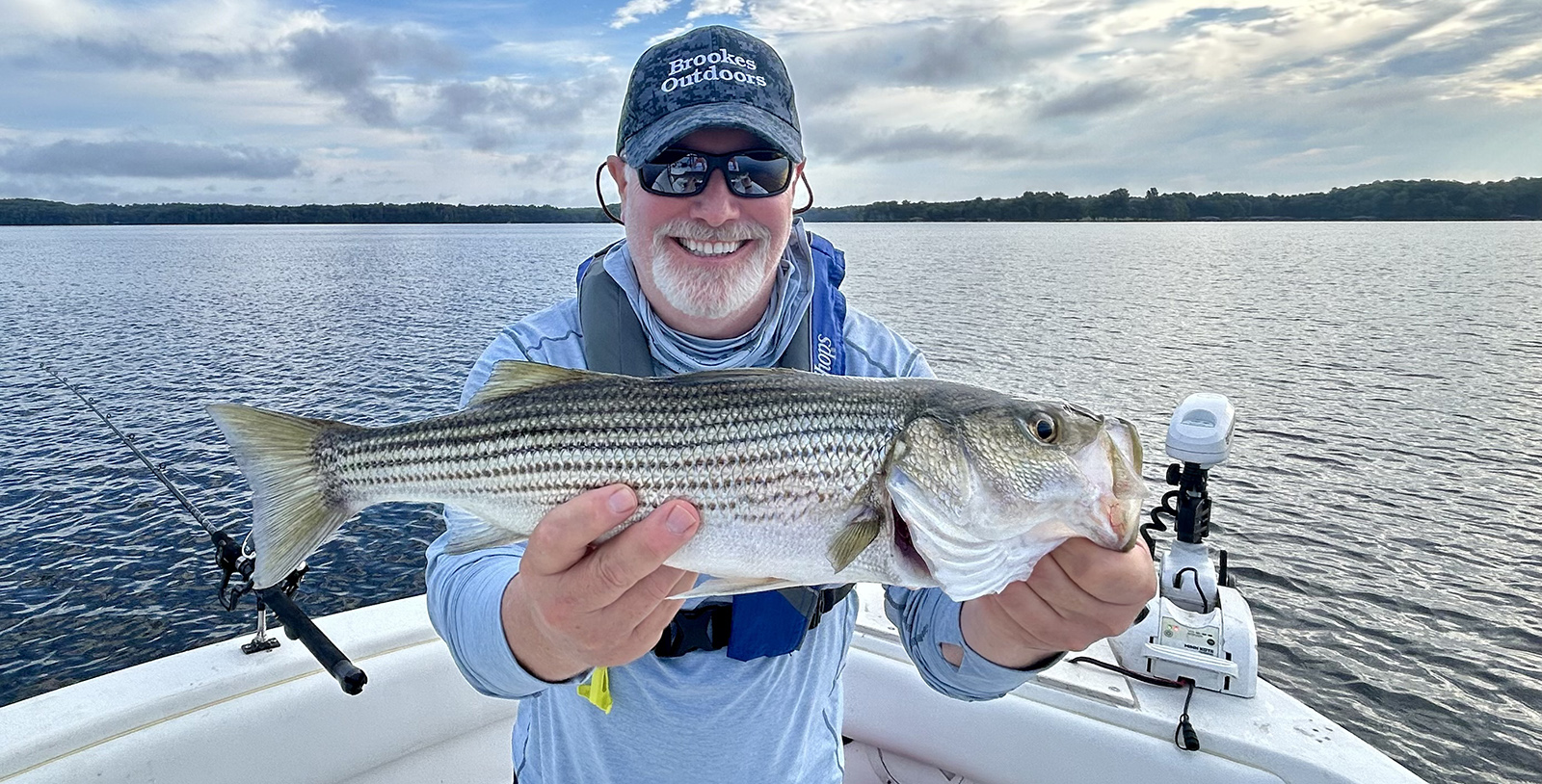一名男子坐在船上，拿起一條大條紋貝斯，微笑。