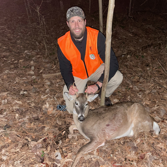 一張身穿鮮豔橙色衣服的男子跪在地上的照片,他面前躺著一隻釘鹿、