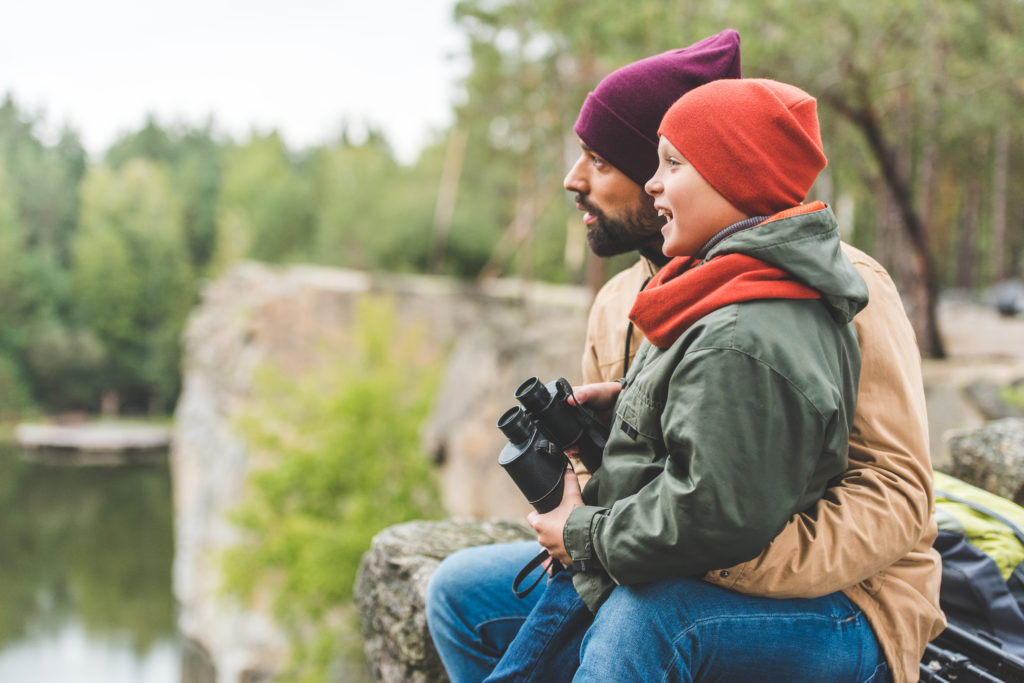 一個男人抱著一個拿著雙筒望遠鏡的孩子的圖像，兩個人正在向左看。